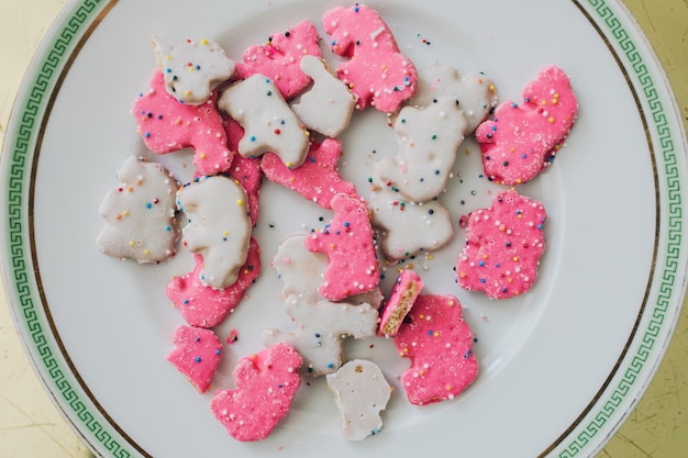 Photo frosted circus animal cookie pink and white sprinkled animal crackers on white plate with green greek key on gold table