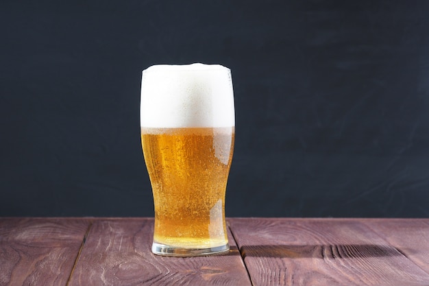 A frosted glass of light beer with a frothy cap on a wooden table