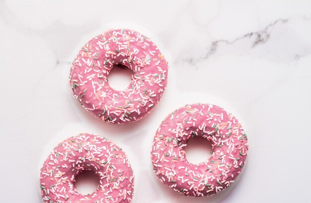 Frosted sprinkled donuts sweet pastry dessert on marble table background doughnuts as tasty snack top view food brand flat lay for blog menu or cookbook design