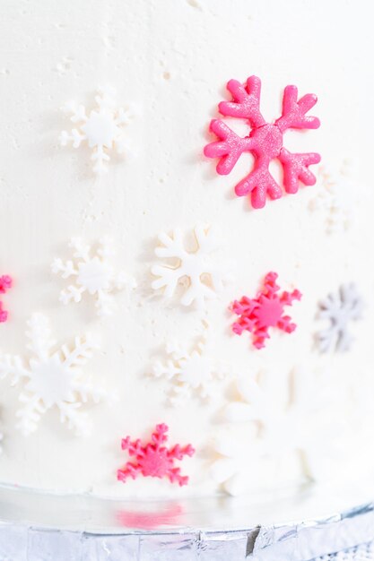 Frosting a tall round cake with white Italian buttercream icing and decorating with fondant snowflakes.