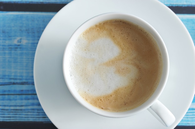 A frothy coffee with cappuccino in a white mug on a blue wooden background 