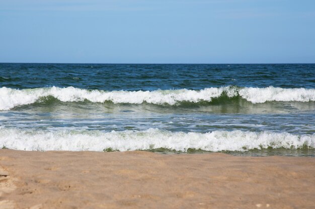 Onde bianche spumeggianti sulla spiaggia sabbiosa del mar baltico. mare blu e cielo blu brillante, alta marea. estate in spiaggia