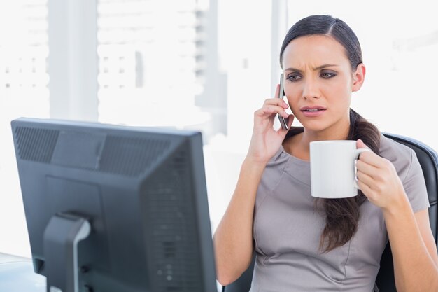 Frowning businesswoman holding coffee and answering phone