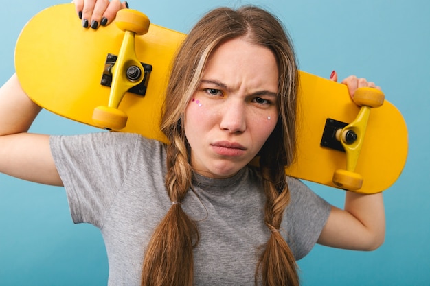 Frowning cute girl standing isolated, holding skateboard