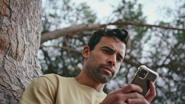 緑の公園でスマートフォンの画面を見ているニュースフィードを見ている眉をひそめる男性