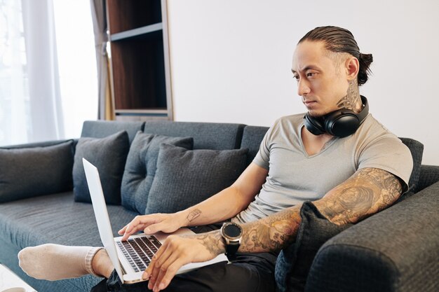 Photo frowning serious mixed-race man sitting on sofa at home and answering e-mails on laptop or coding