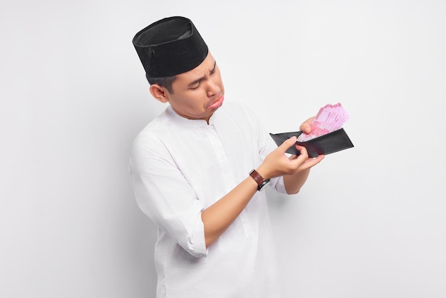 흰색 배경에 고립 된 지갑에 현금 돈을보고 인상을 찌푸리고 젊은 아시아 이슬람 남자 사람들 종교 이슬람 라이프 스타일 개념