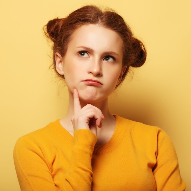 Frowning young redhair woman thinking on yellow background