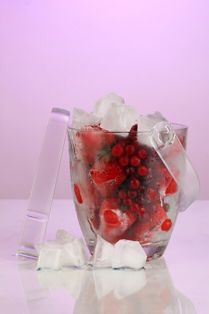 Замороженные ягоды в ведре со льдом на цветном фоне