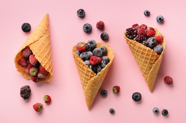 Frozen berries - strawberry, blueberry, blackberry, raspberry in waffle cones on pink background. 
