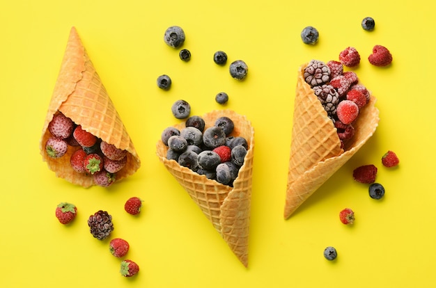 Frozen berries - strawberry, blueberry, blackberry, raspberry in waffle cones on yellow background. 