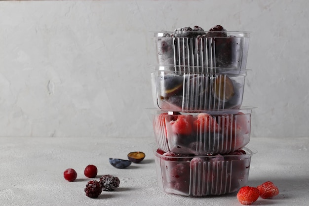 Frozen berries such as cherries strawberries plums and blackberries in the storage boxes on the concrete gray background Copy space