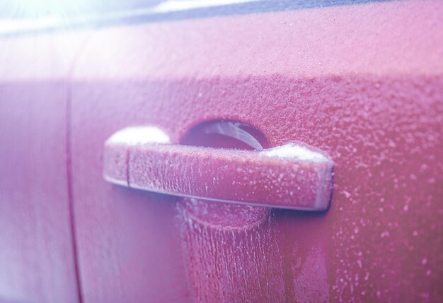 Frozen car door automobile car door or lock is frozen shut\
closeup of car red door handle and lock covered in ice during\
winter storm concept of winter driving preparedness and safety