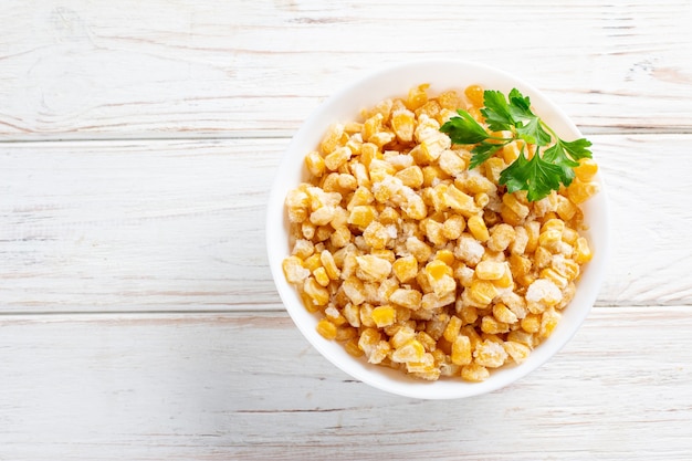 Frozen corn in a plate on white wooden table