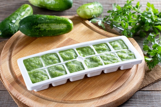 Frozen cucumber puree in ice cube trays ready for freezing on a cutting board on a wooden table. Frozen Food Concept.