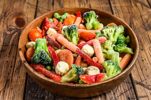 Frozen cut Vegetables, broccoli, sweet peppers, tomatoes, carrots, peas and corn. wooden table. top view.