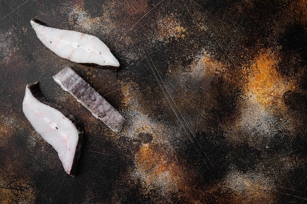 Frozen fillets of white fish, pollock set, on old dark rustic table background, top view flat lay, with copy space for text