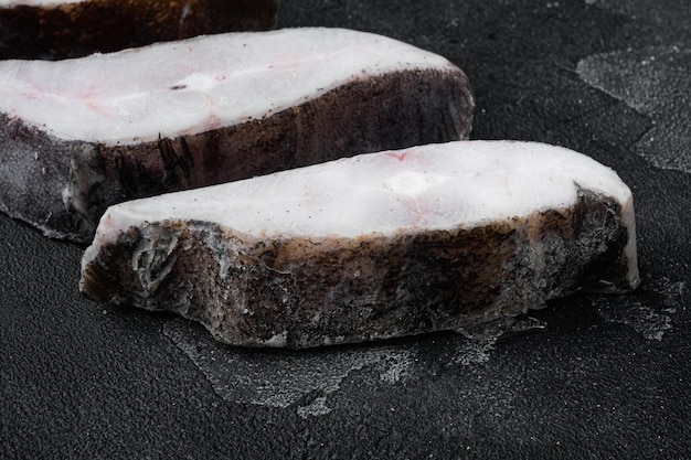 Frozen fish steak on black dark stone table background