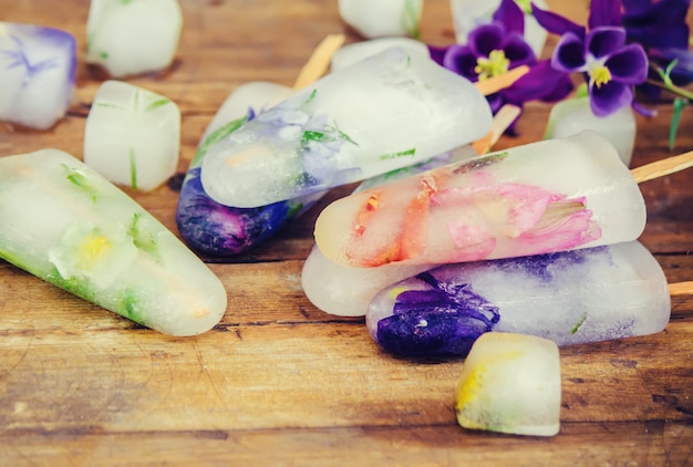 Frozen flowers in ice cubes and ice cream on a stick. selective focus.