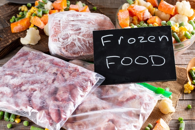 Frozen Food. Assortment of frozen vegetables and meat on wooden table.