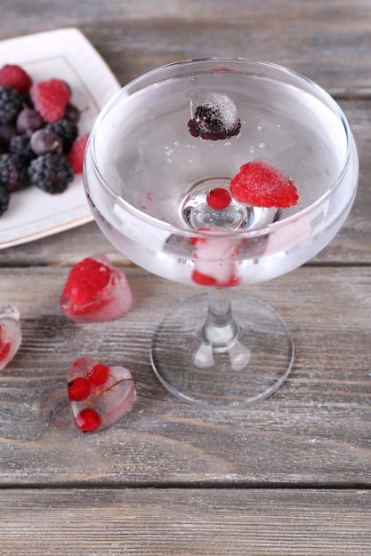 Frozen forest berries on plate and cocktail with berries frozen in ice cubes on wooden table background