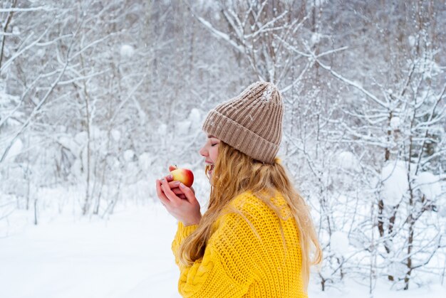 Frozen girl against the winter landscape wants to bite off a piece of apple