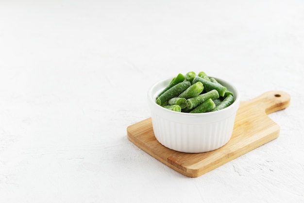 Frozen green beans in a bowl on a wooden board