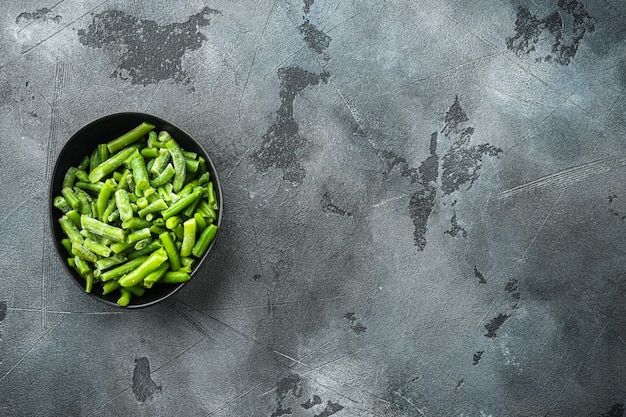Frozen green beans set, in bowl, on gray stone table, top view flat lay