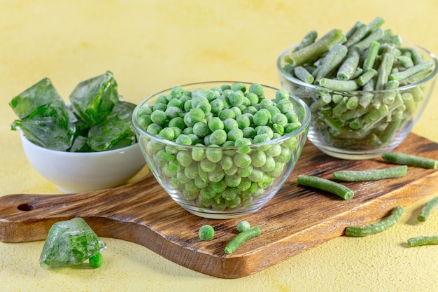 Frozen green peas, string beans, ice cubes with fresh parsley on a wooden board