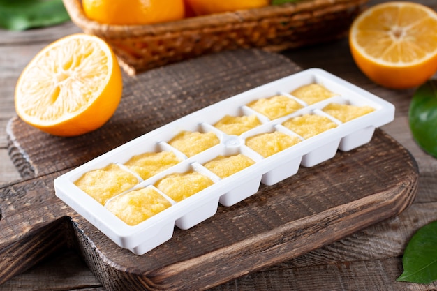 Frozen Lemon Juice cubes in tray on a wooden table, closeup