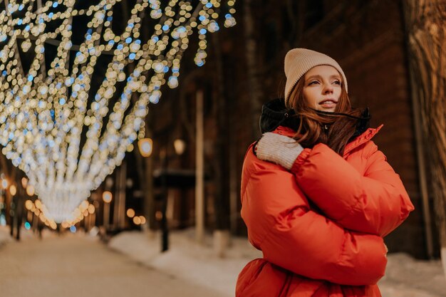 Frozen lonely young woman in hat and winter jacket hugging arms around herself trying to keep warm