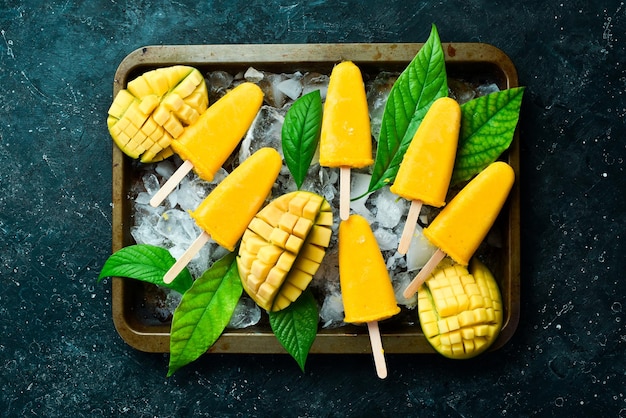 Frozen mango popsicles on a tray Cold summer sweets On a black stone background Top view