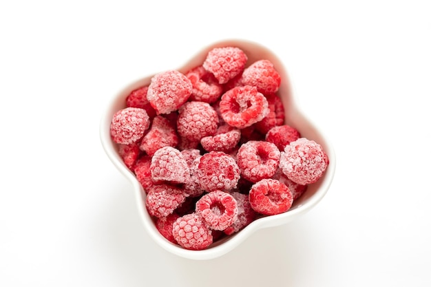 Frozen organic raspberry in white bowl on white background View from above