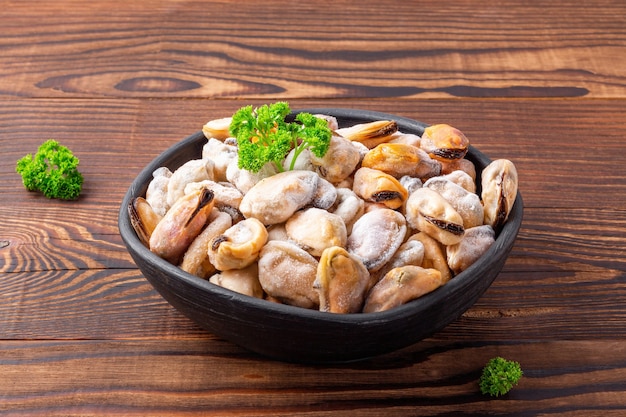 Frozen peeled shellfish with green parsley in a black dish on wooden background, closeup.