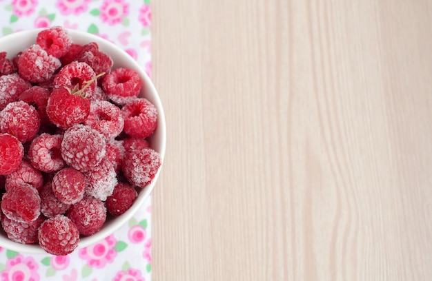 Photo frozen raspberries in a white bowl on wooden background with free copy space