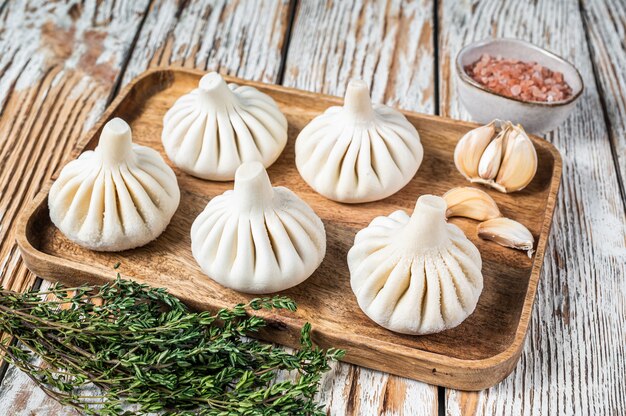 Frozen Raw dumplings Khinkali with beef and lamb meat on wooden tray with herbs