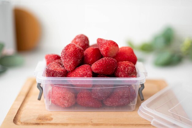 Frozen ripe strawberries in a plastic container closeup