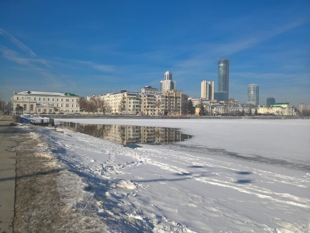 Frozen river by buildings against sky in city during winter