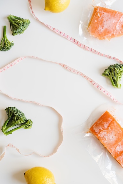 Frozen salmon fish fillets in plastic package fresh broccoli\
lemons and measuring tape