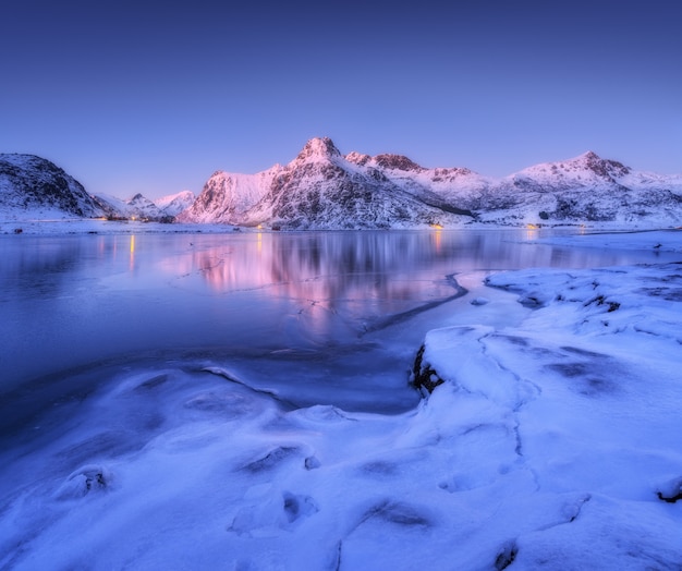 Frozen sea coast and beautiful snow covered mountains in winter at dusk