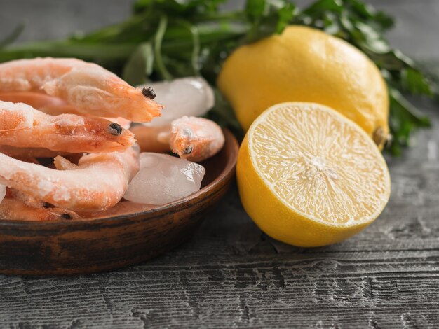 Frozen shrimp with lemon and herbs on clay bowl on black wooden rustic table