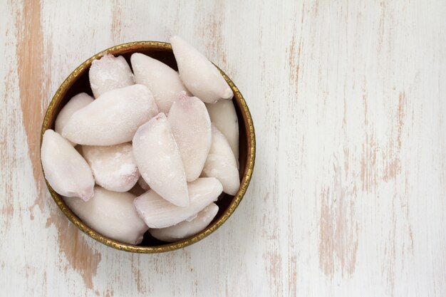 Frozen squids in dish on white wooden surface