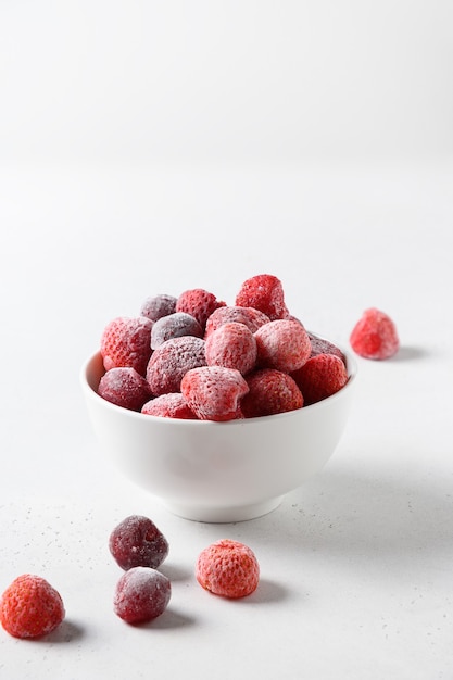 Frozen strawberries and cherry in bowl on white background