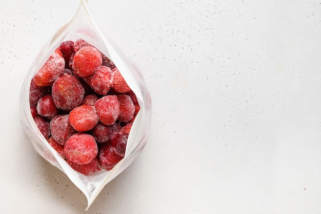 Frozen strawberries in plastic packet on white view from above