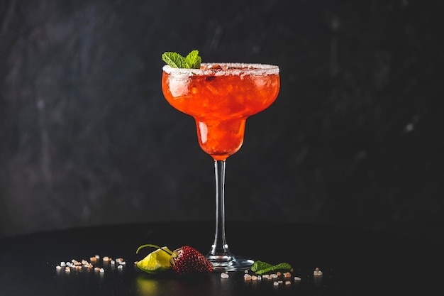 Frozen strawberry lime mint margarita in tall footed glass on the dark background Luxury alcohol fresh drink