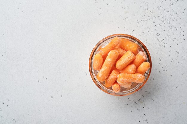 氷とコピースペースのあるコンクリートの灰色のテーブルの上のガラスのボウルに冷凍野菜の赤ちゃんのニンジン。