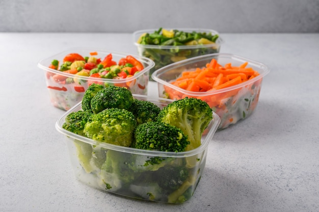 Frozen vegetables carrot broccoli spinach green pods beans in plastic trays on gray surface