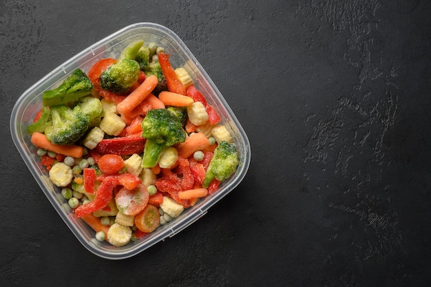 Frozen vegetables in container on black background top view