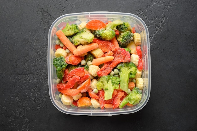 Frozen vegetables in container on black background top view