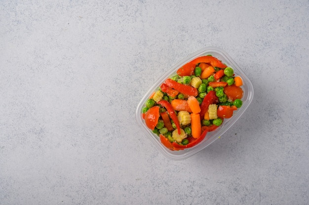 Frozen vegetables corn red pepper peas carrots tomatoes in plastic tray on an gray surface top